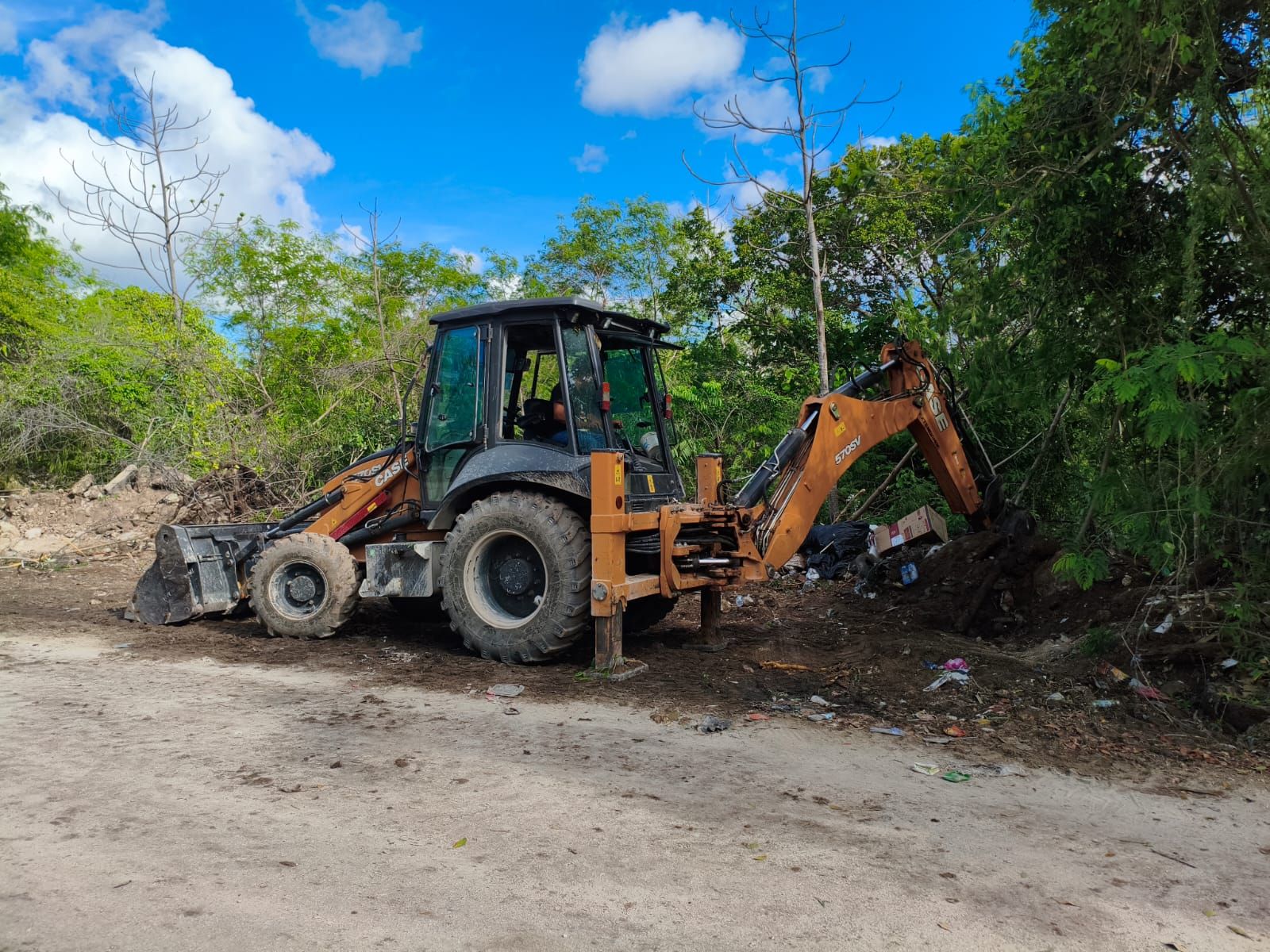 Retroexcavadora con estabilizadores desplegados en la limpieza de un terreno